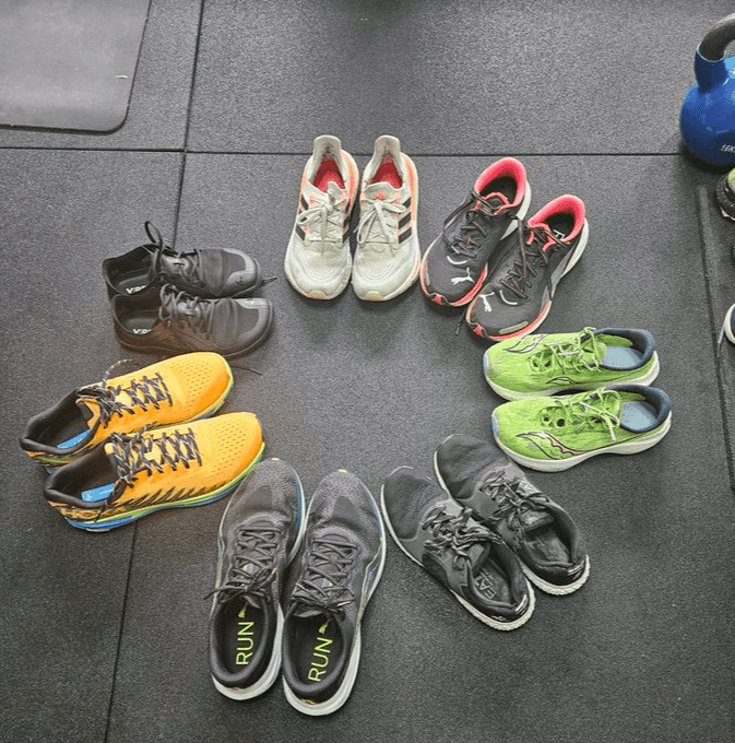 Circle of various running shoes arranged on a gym floor, with pairs in different colors and designs.